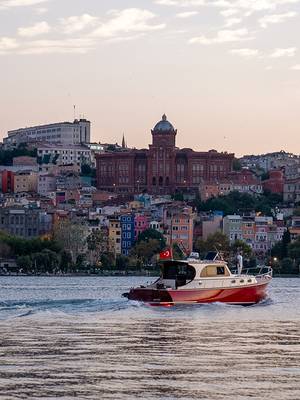 Łódź płynąca po Złotym Rogu w pobliżu hotelu Rixos Tersane Istanbul, z historycznym greckokatolickim kolegium Fener i kolorowymi domami Balat w tle.