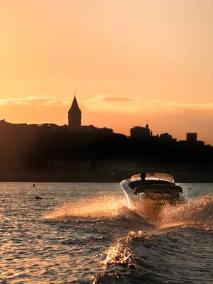 Rejs łodzią motorową o zachodzie słońca w pobliżu hotelu Rixos Tersane Istanbul, z sylwetką wieży Galata Tower świecącą na tle złocistego nieba.