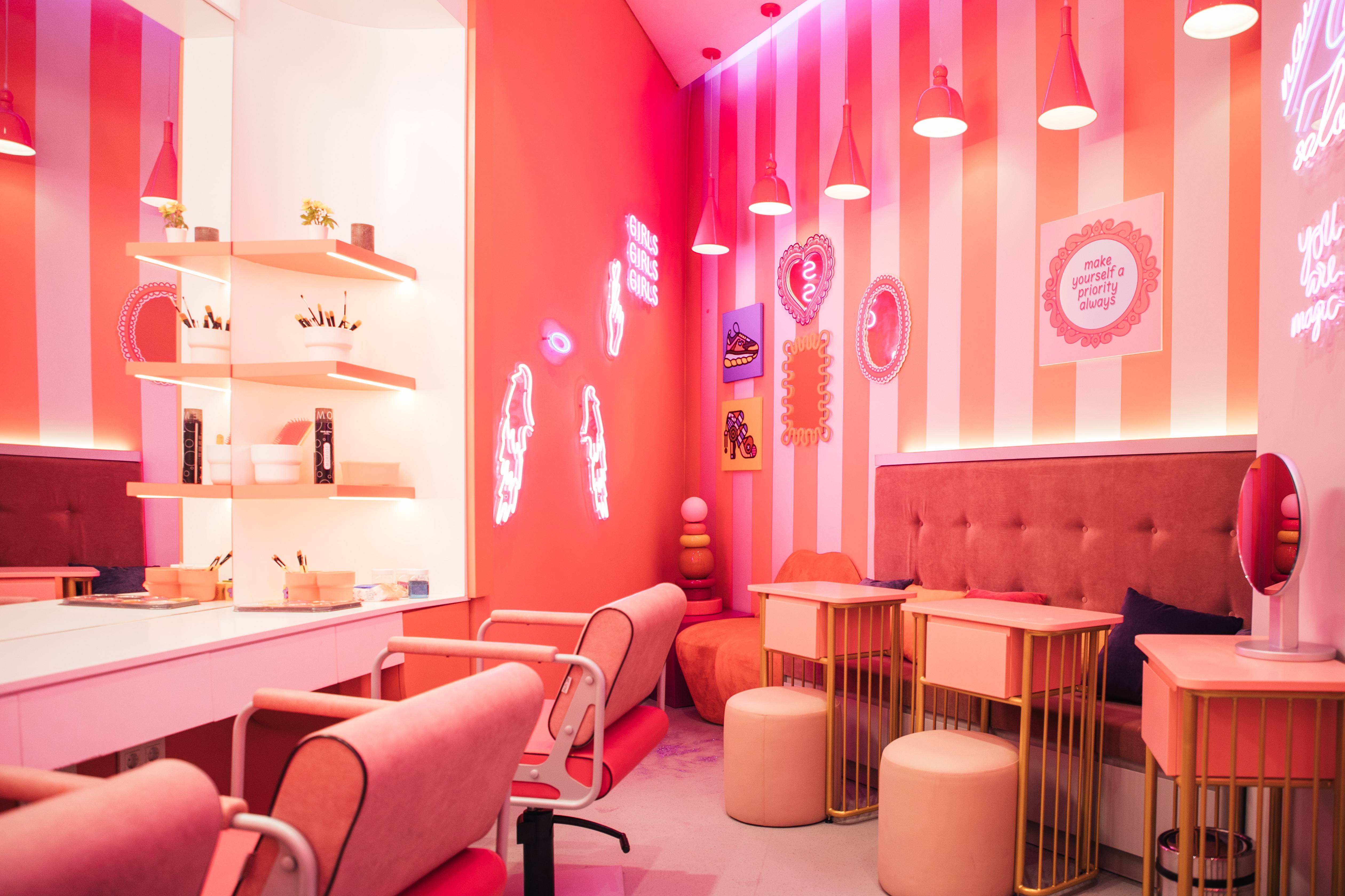 A vibrant, pink-themed beauty salon inspired by Candy Candy at Rixos Tersane Istanbul, with plush chairs, manicure tables, striped walls, neon signs, and bright pendant lights, creating a playful and inviting atmosphere.