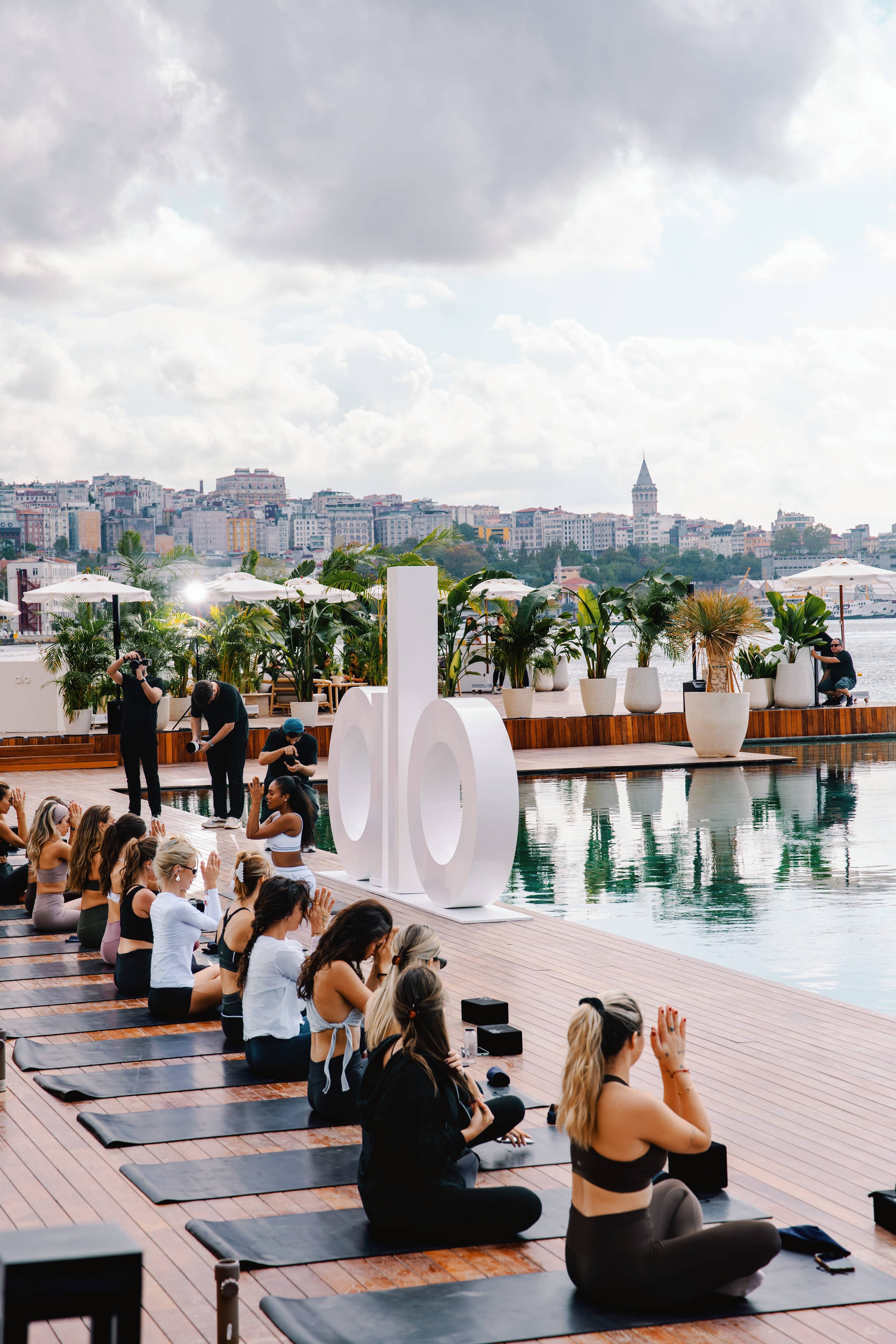 Group yoga session by the waterfront pool at Rixos Tersane Istanbul with a city view in the background.