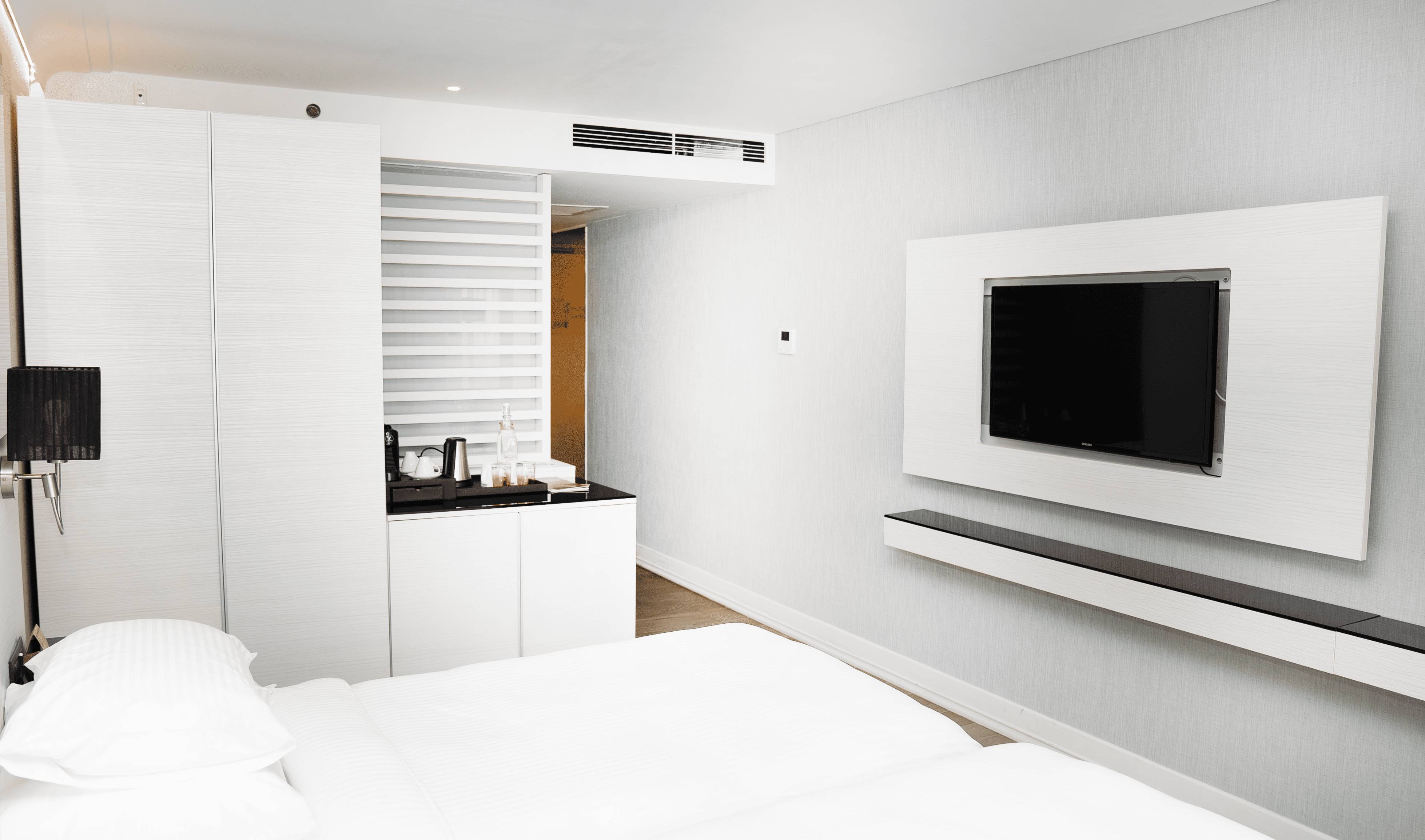 Moderna hotelska soba s bračnim krevetom, bijelim ormarićem/kutijom za kavu i zidnim televizorom.