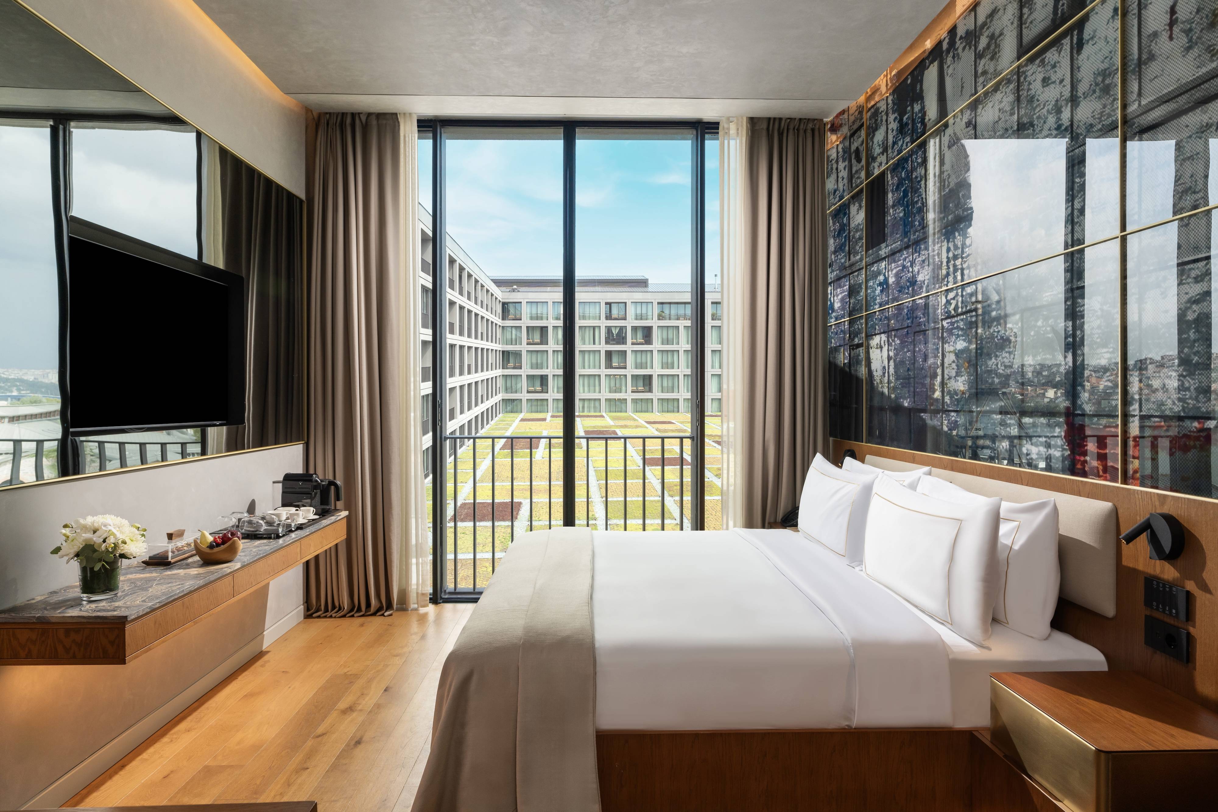Ten nowoczesny apartament typu junior suite z częściowym widokiem na morze w obiekcie Rixos Tersane Istanbul wyposażony jest w duże łóżko z białą pościelą, telewizor na ścianie, ekspres do kawy oraz sięgające od podłogi do sufitu okna z widokiem na dziedziniec i panoramę miasta.