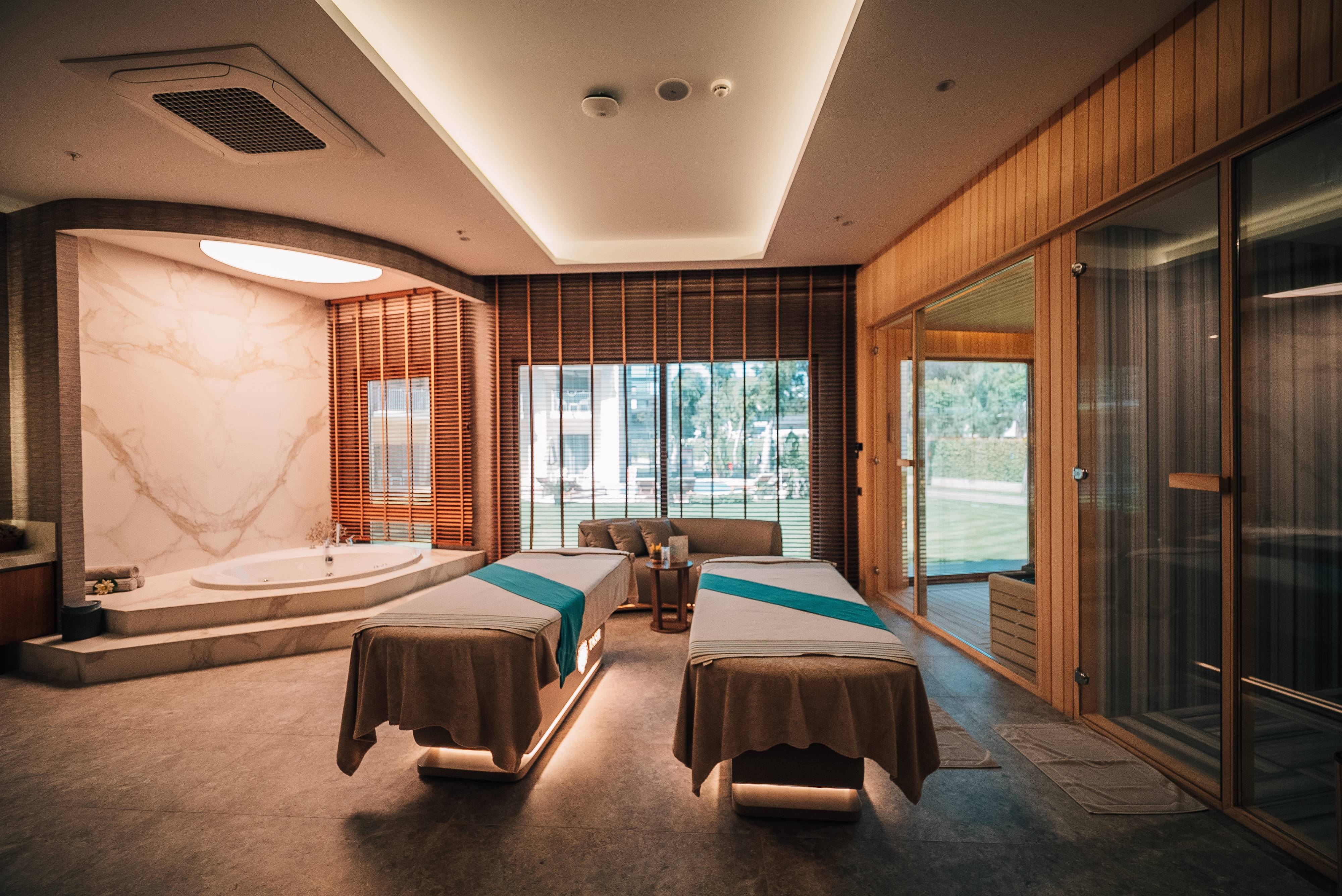 Spacious VIP spa room at Anjana Spa, Rixos Park Belek, featuring massage beds, private sauna and tranquil garden views through large glass windows.