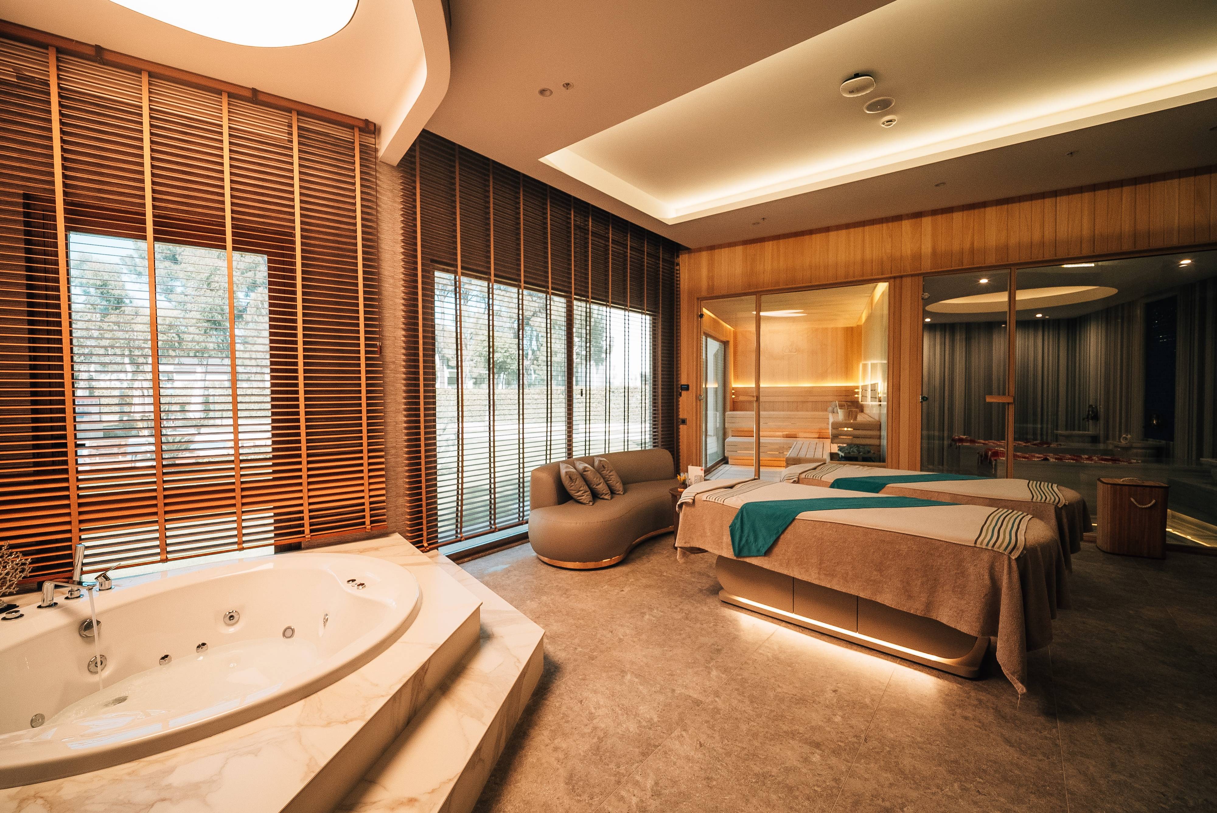 Elegant VIP spa suite at Anjana Spa, Rixos Park Belek, with jacuzzi, twin massage beds and floor-to-ceiling windows overlooking the garden.
