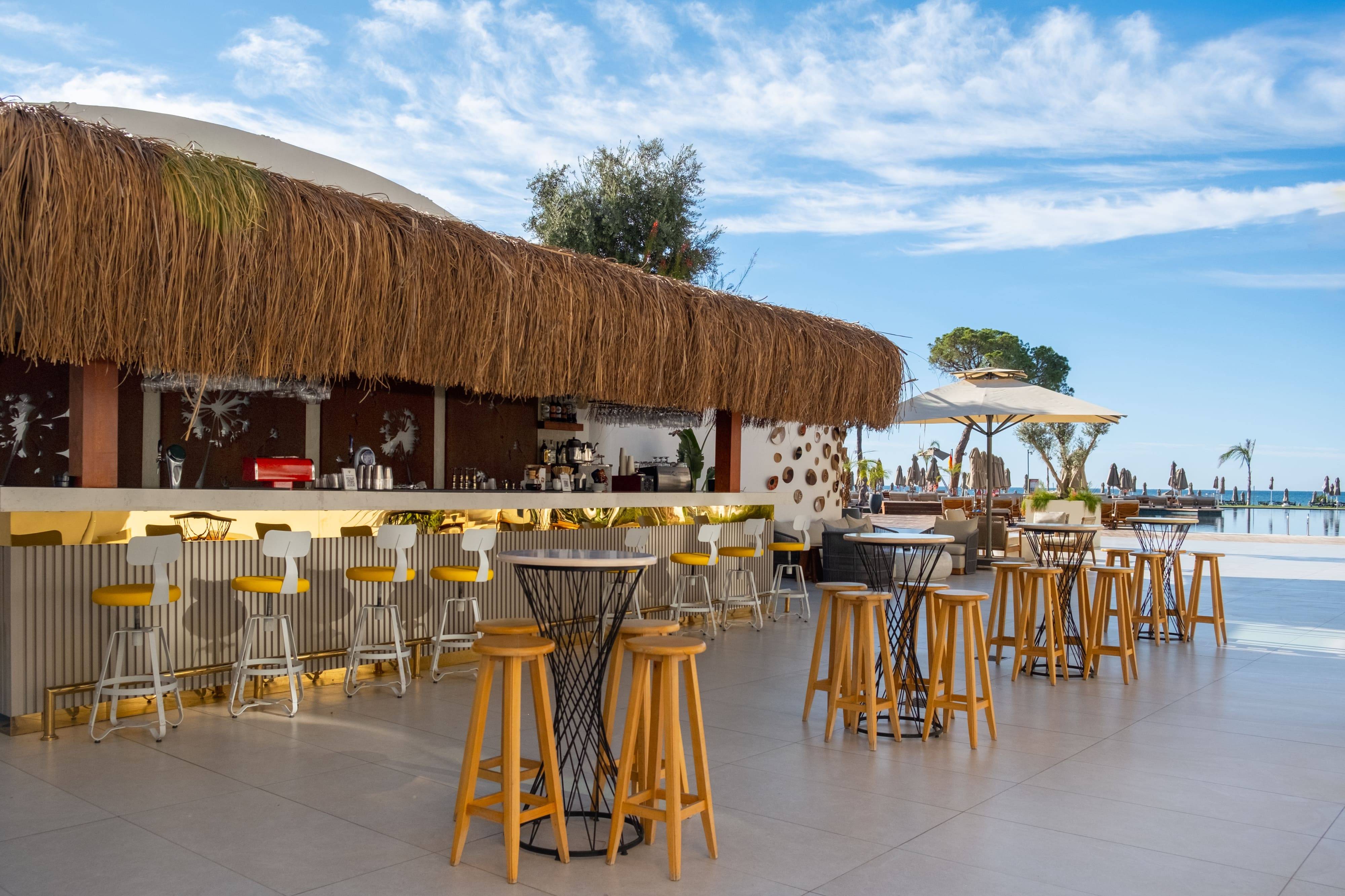 Outdoor Pool & Chill Bar at Rixos Park Belek featuring straw-roof design, bar stools, and sea-view terrace.