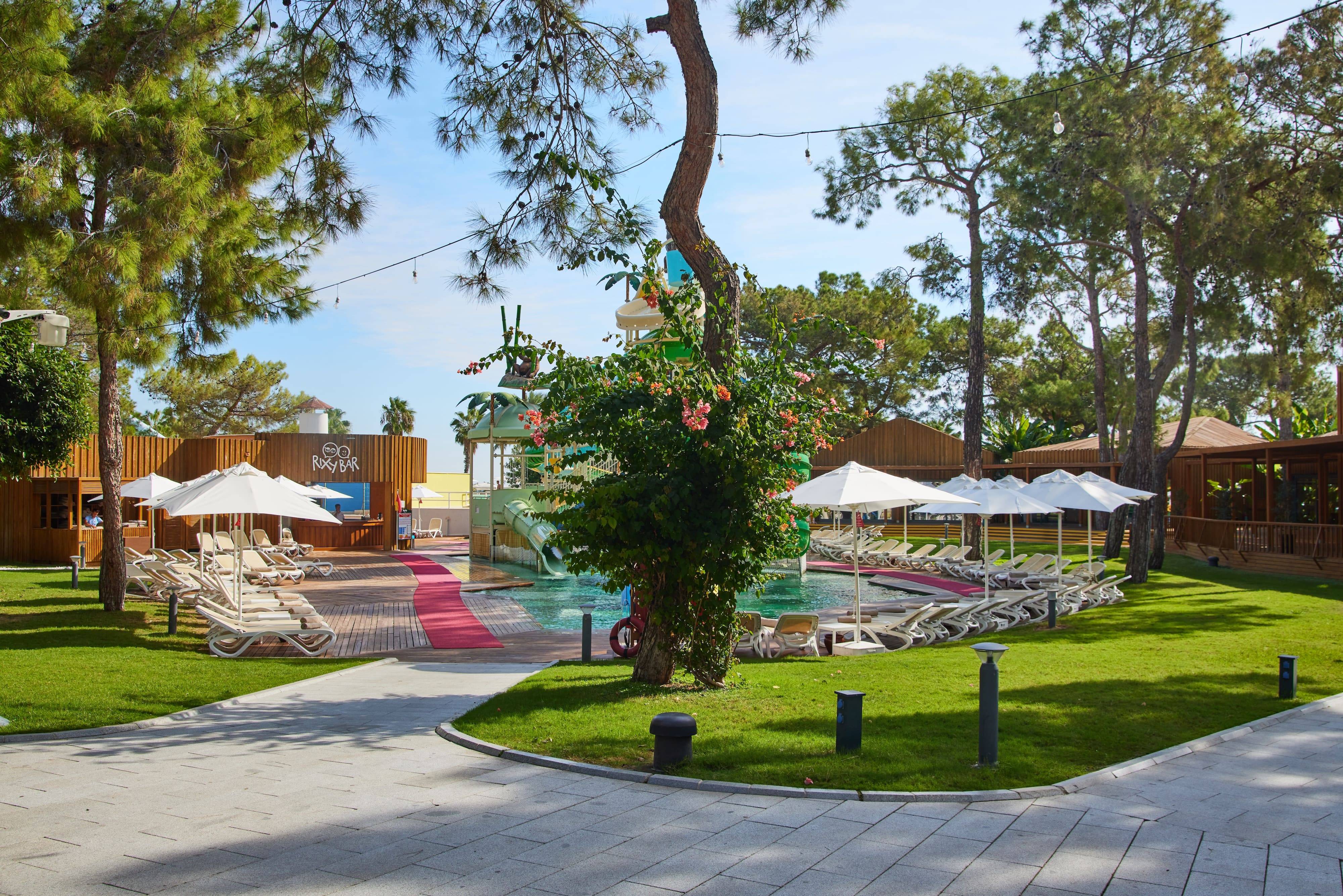 Rixy Pool Bar at Rixos Sungate surrounded by sun loungers, umbrellas, and lush greenery near the kids’ water slides.