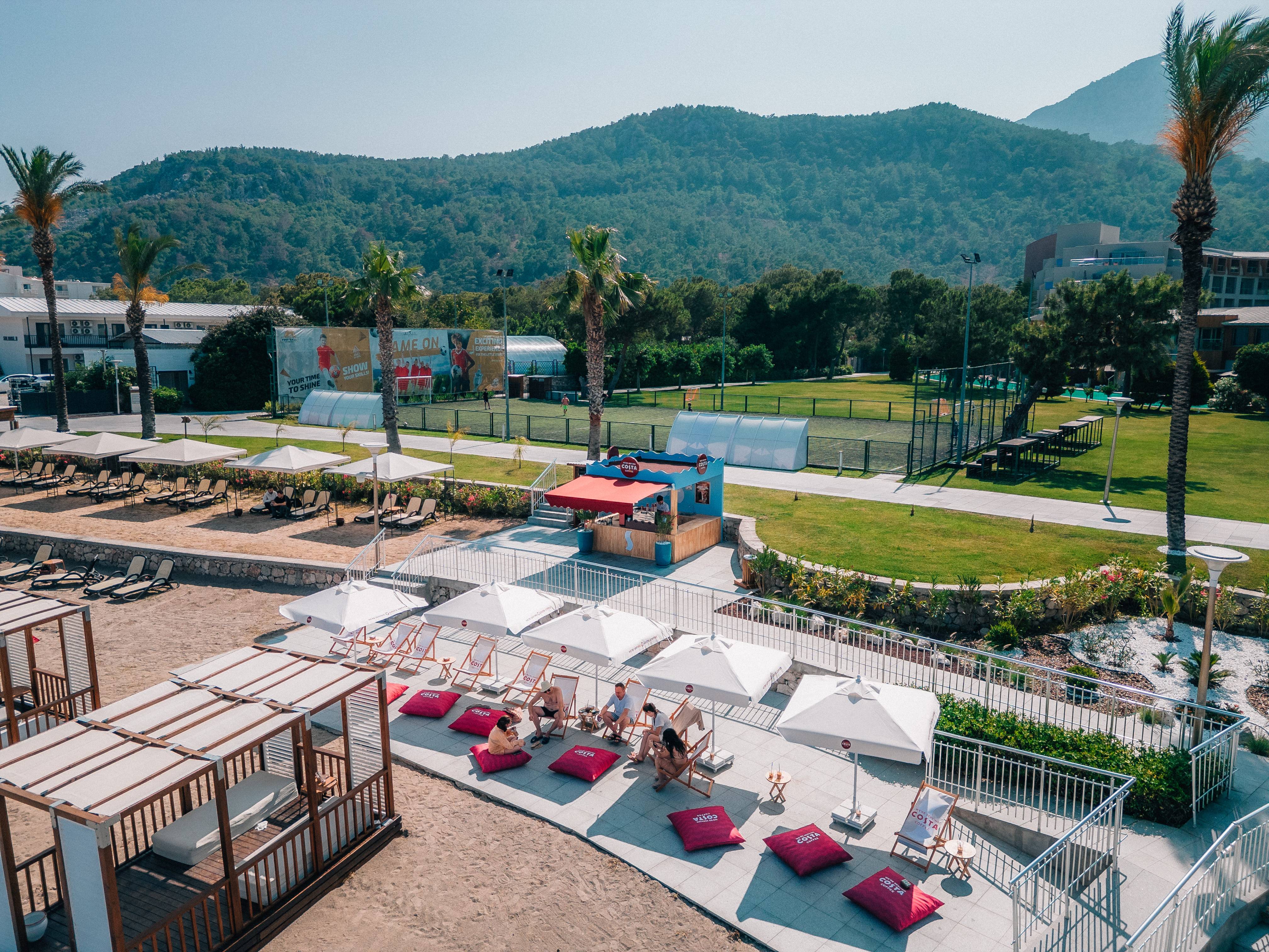 Costa Coffee lounge area at Rixos Sungate, featuring sunbeds, umbrellas, and a scenic mountain backdrop.