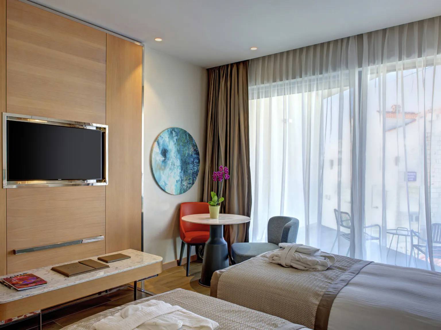 Moderna soba s dva odvojena kreveta s ogrtačima, malim prostorom za sjedenje i velikim prozorom s prozirnim i teškim zavjesama.