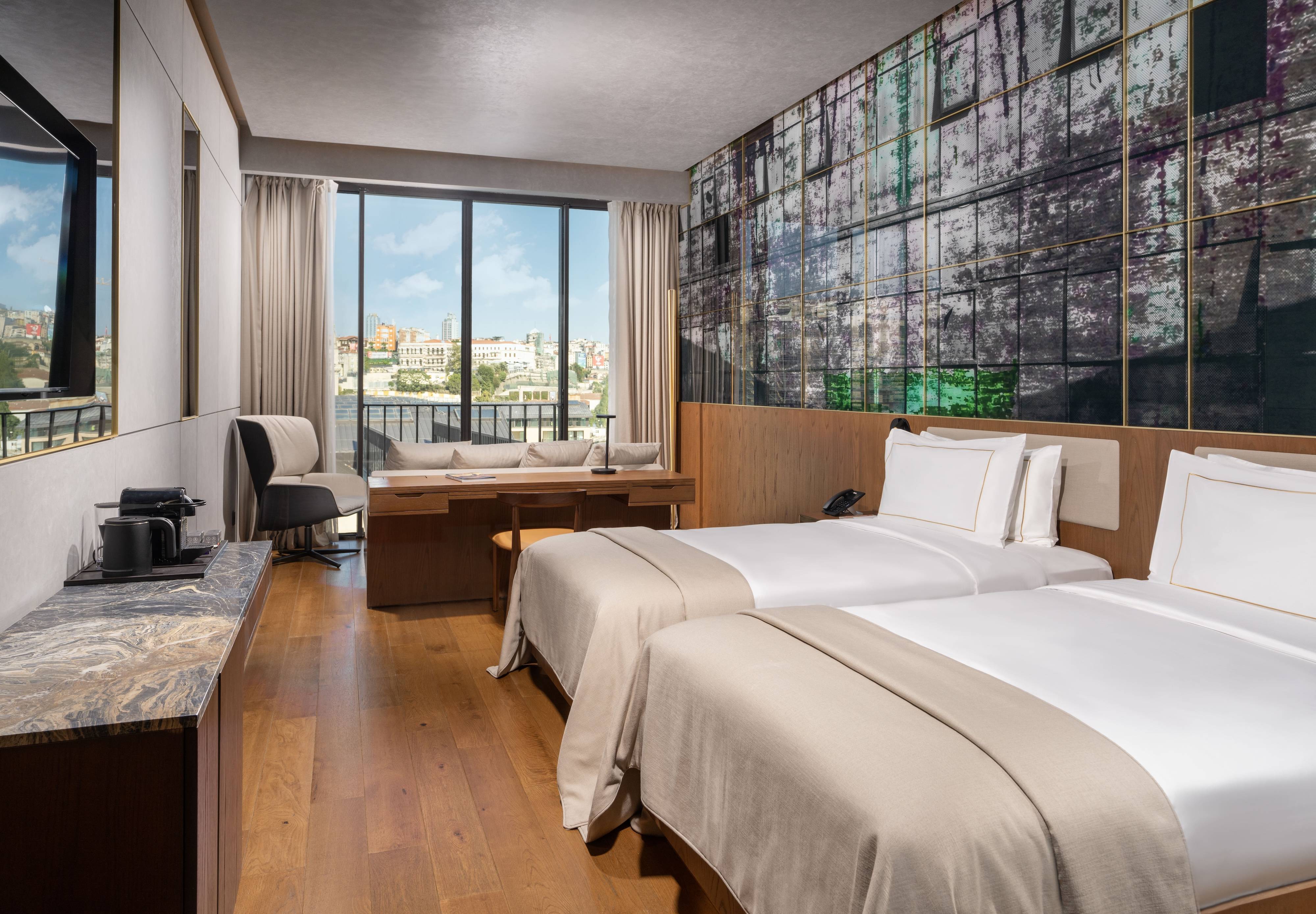 Pokój rodzinny z dwiema sypialniami i częściowym widokiem na morze w hotelu Rixos Tersane Istanbul to nowoczesna przestrzeń z dwoma łóżkami pojedynczymi, marmurową konsolą, ekspresem do kawy, dużym oknem z widokiem na miasto, przytulną częścią wypoczynkową i kolorową ścianą z abstrakcyjnymi akcentami.
