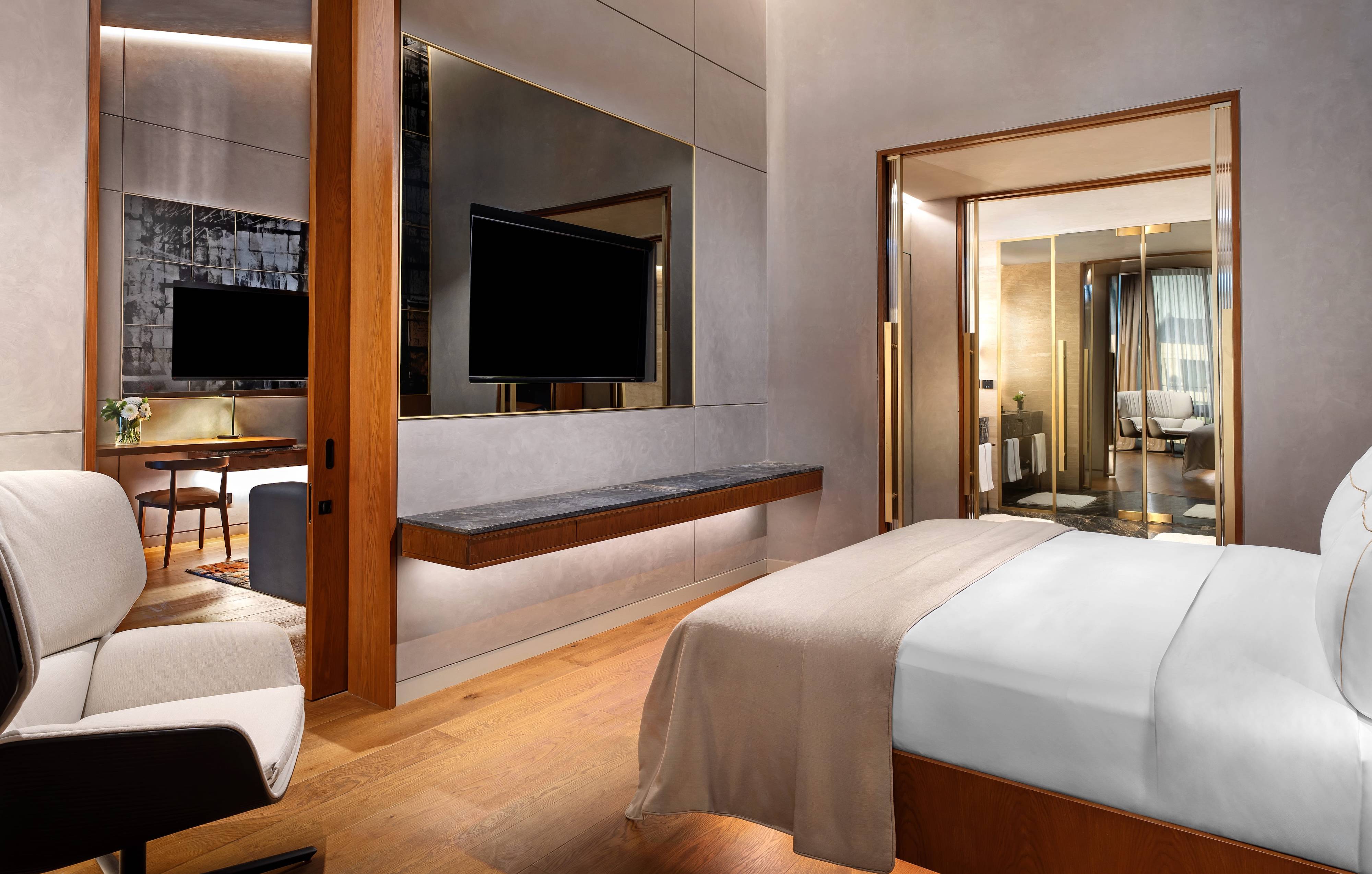 Jest to nowoczesny pokój hotelowy z dużym łóżkiem, drewnianymi podłogami, telewizorem na ścianie oraz stylową łazienką z marmurowymi akcentami i naturalnym oświetleniem.