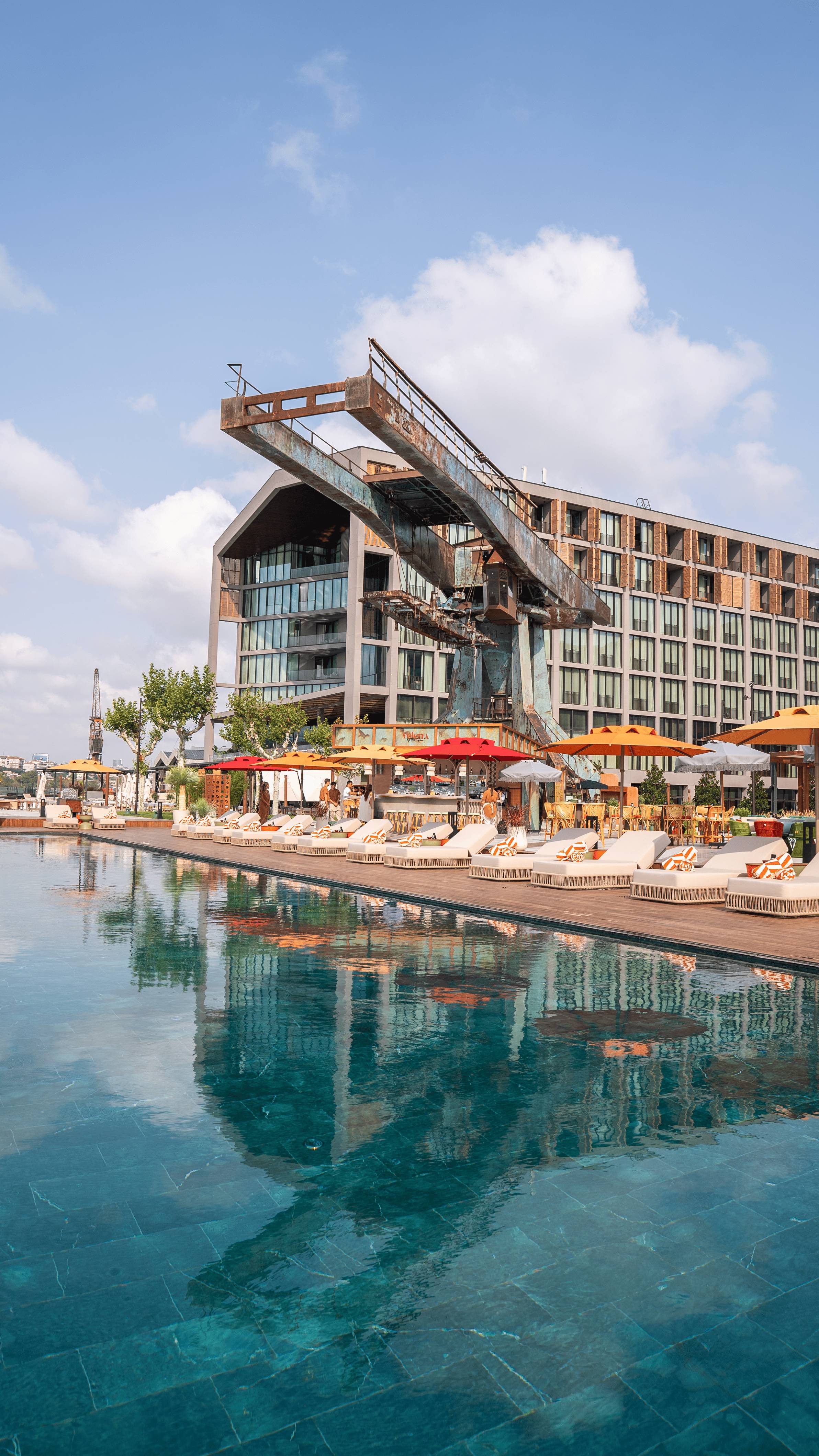 Rixos Tersane Istanbul przy basenie z nowoczesną architekturą przemysłową i leżakami odbijającymi się w wodzie