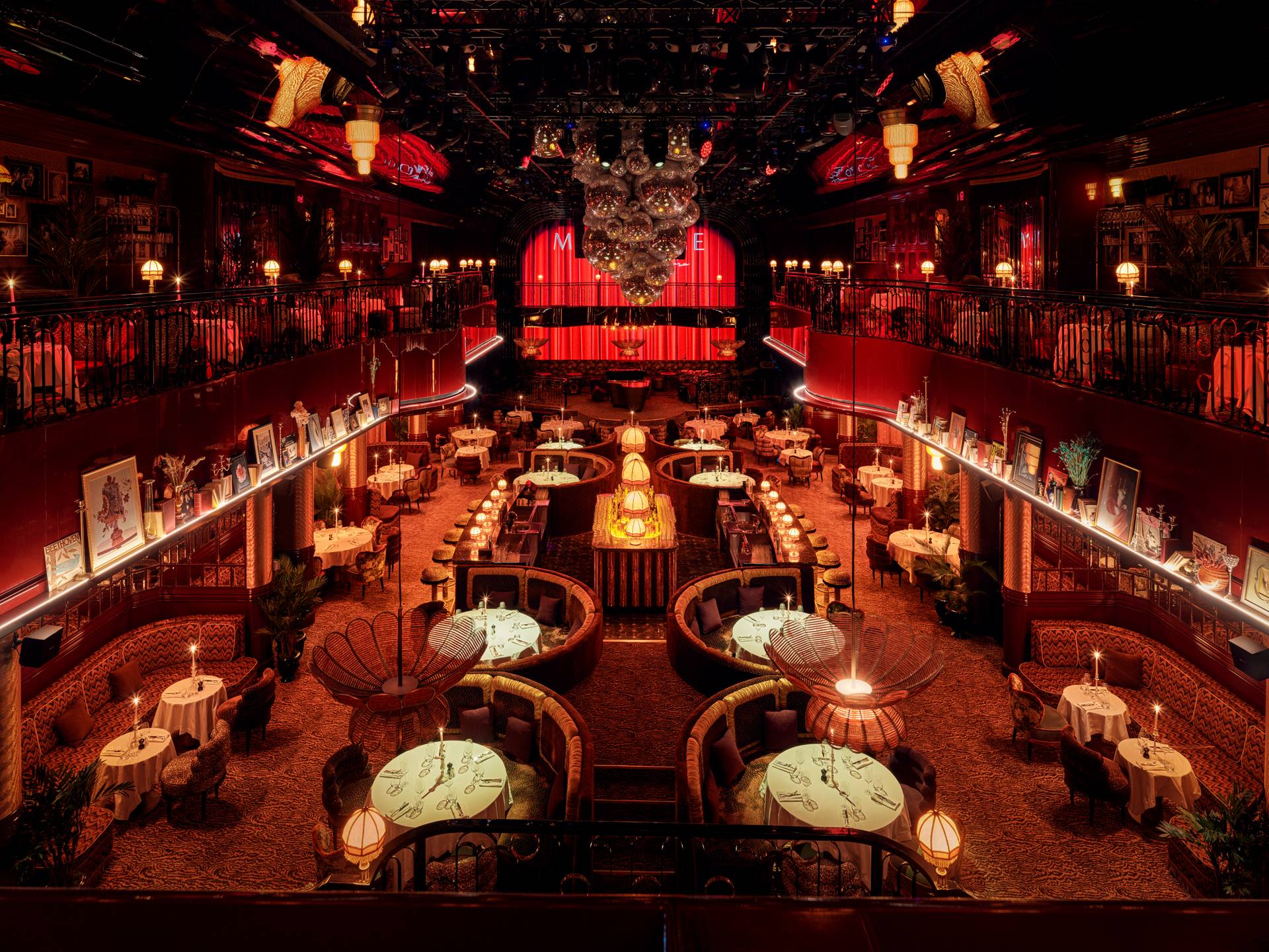 Elegancka restauracja w stylu teatralnym w Rixos Tersane Istanbul z pluszowymi, zakrzywionymi kabinami, okrągłymi stołami, ciepłym oświetleniem, żyrandolami i podświetlaną na czerwono sceną. Wystrój jest zabytkowy i luksusowy, przywołując na myśl A Vivid Story of Bohemian Spirit w czarującej, zachęcającej atmosferze.