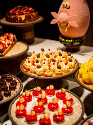 Wykwintny stół z deserami podczas niedzielnego brunchu w hotelu Rixos Tersane Istanbul, na którym prezentowane są pięknie wykonane wypieki i mini ciastka z bitą śmietaną, jagodami i czekoladą, artystycznie ułożone obok zabawnej dekoracyjnej kompozycji.