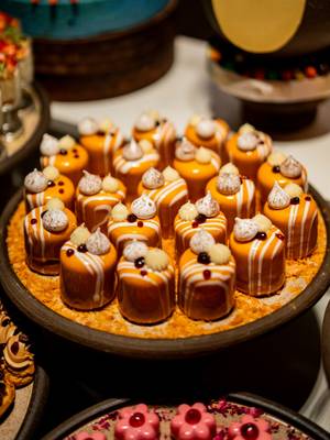 Kusząca ekspozycja deserów podczas niedzielnego brunchu w hotelu Rixos Tersane Istanbul, na której eleganckie mini ciastka pokryte pomarańczową polewą, zwieńczone bitą śmietaną i dekoracyjnymi dodatkami, są pięknie ułożone na talerzu, aby goście mogli się nimi delektować.