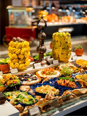 W Rixos Tersane serwowany jest bogaty bufet niedzielnego brunchu, na którym można znaleźć różnorodne kolorowe sałatki, przystawki i dania meze ułożone w ozdobnych niebieskich miskach, a elegancką prezentację dopełniają artystyczne dekoracje w kolorze cytrynowym i żółtym.