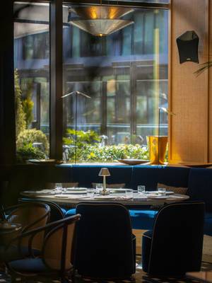 Intérieur de l'Em Sherif au Rixos Tersane Istanbul, avec une élégante table ronde, des chaises en velours bleu somptueux, un sol carrelé géométrique et une vue sur la verdure à travers de grandes baies vitrées.