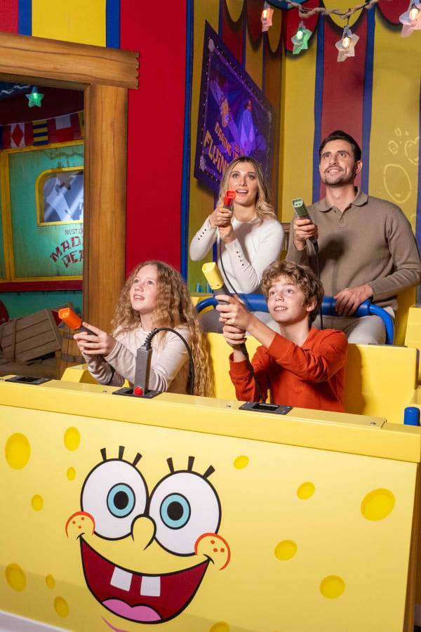 Стамбулдағы Rixos Tersane қонақ үйіндегі Nickelodeon Play ойын-сауық орталығында сары түсті Губка Боб тақырыбындағы көлікте отырған төрт адамнан тұратын отбасы. Ата-аналар мен балалар интерактивті ойын құрылғыларын ұстап, аттракционның экрандарына қуана қарап тұр.