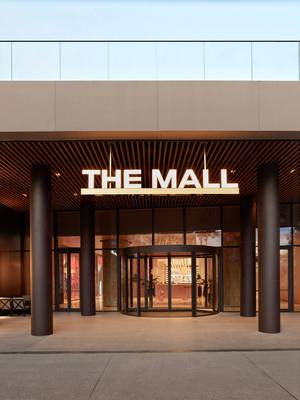 L'entrée moderne du centre commercial The Mall at Rixos Tersane Istanbul, avec une grande enseigne lumineuse « THE MALL » suspendue à un plafond à lattes de bois au-dessus d'une porte tournante en verre et de colonnes sombres.