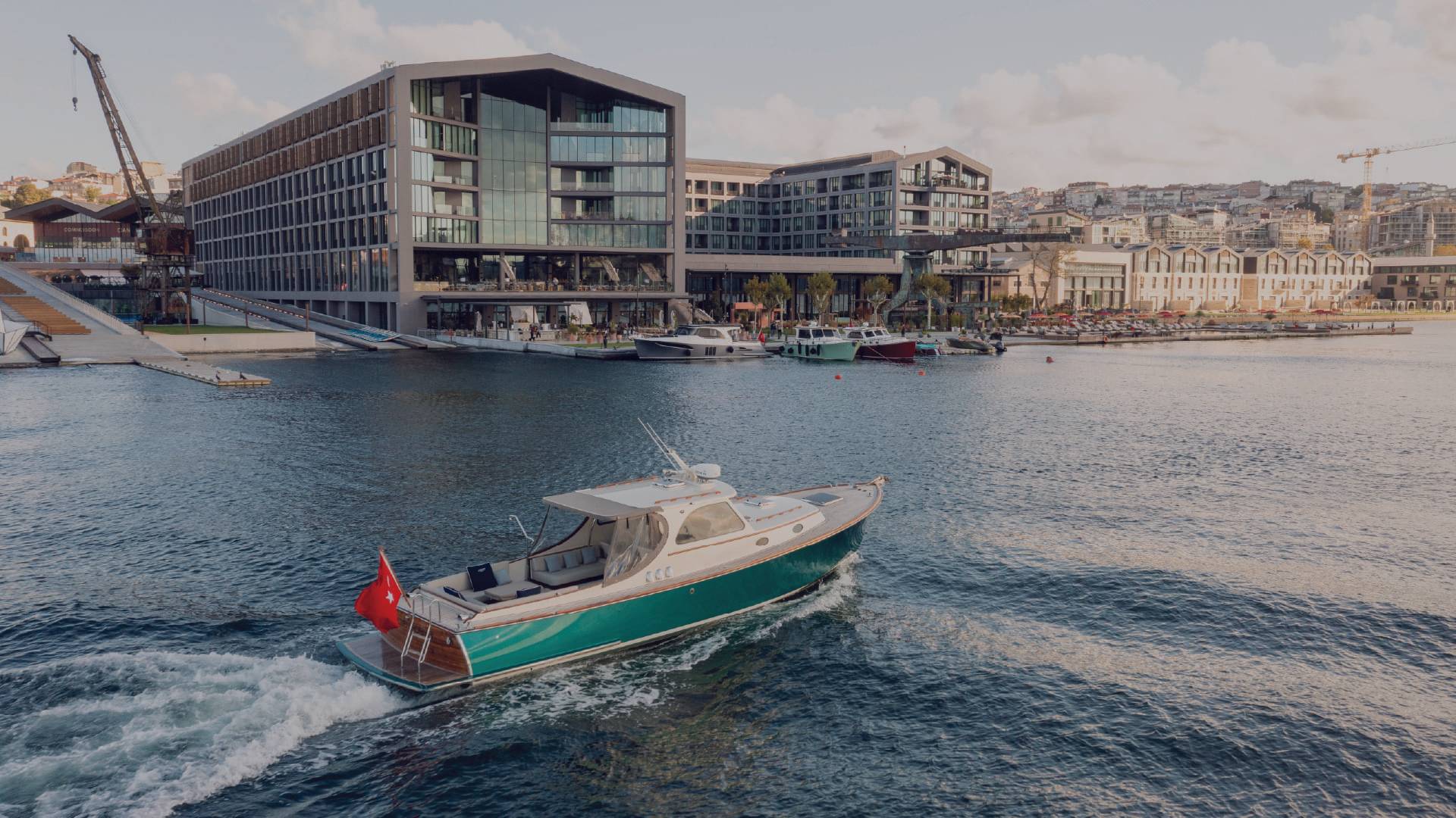Luxury motor yacht sailing in front of Rixos Tersane Istanbul hotel along the Golden Horn with modern waterfront architecture in the background