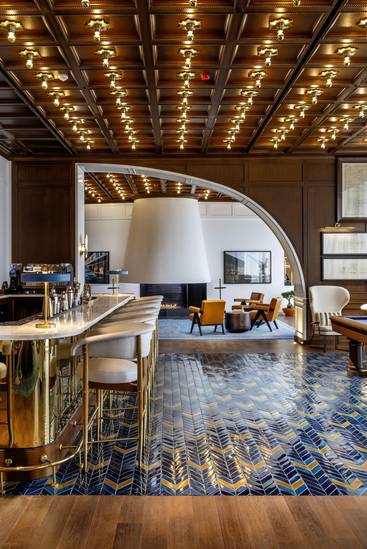 A luxurious lounge at Rixos Tersane Istanbul features a brass bar with white stools, blue patterned tile floor, wood-paneled ceiling with many lights, a billiards table, and a modern fireplace with seating in the Gowden Club.