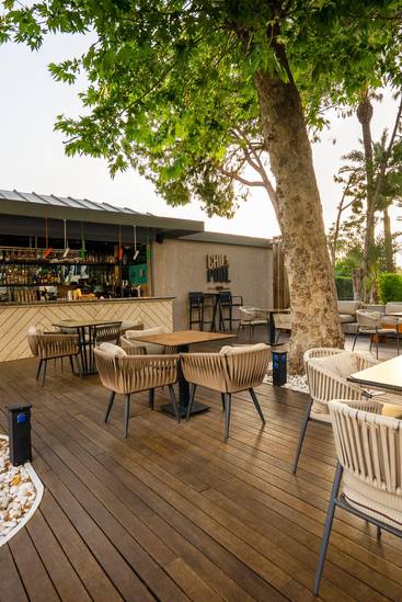 Rixos Downtown Antalya'da gölgeli ağaçların altında rahat bir açık hava oturma alanına sahip Chill & Pool Bar