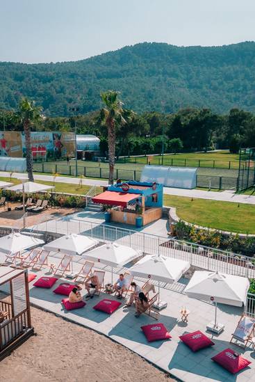 Rixos Sungate-тегі Costa Coffee залы, шезлонгтары, қолшатырлары және әдемі тау фоны.